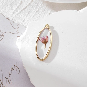 Close-up of handmade oval gold frame pendant with real pink dried flower in clear resin