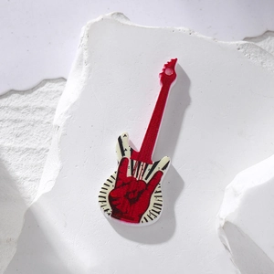 Detail of red rock gesture acrylic electric guitar charm on a white stone surface