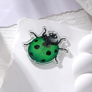 Macro detail of a green glitter acrylic ladybug pendant on a white stone background