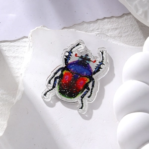 Macro shot of gradient colorful acrylic beetle pendant with silver glitter on white stone