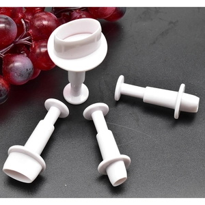 Detail of four white plastic oval spring-loaded plunger cutters for baking on dark surface