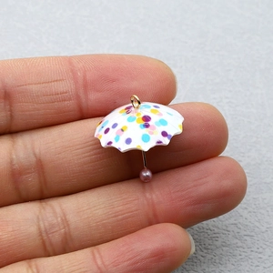 Mini ciondolo a ombrello in acrilico con pois colorati e anello d'oro tra le dita