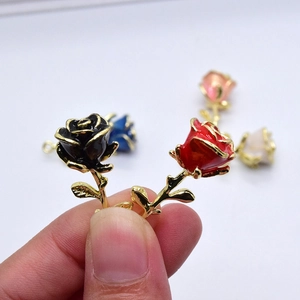 Mano che tiene ciondoli a rosa in smalto rosso e nero con steli dorati per gioielli fai-da-te