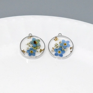 Détail de pendentif rond en résine avec fleurs séchées bleues et feuilles d'or en argent
