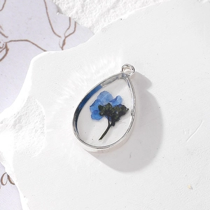 Detail of teardrop resin pendant with real blue dried flowers and silver metal edge