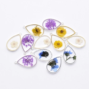 Macro detail of teardrop resin pendants with embedded dried flowers and alloy frames