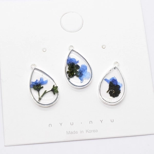 Detailed close-up of water drop resin pendants with blue dried flowers and silver frames