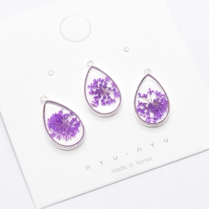 Macro detail of three teardrop pendants with purple dried flowers in resin charms