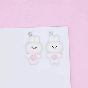 Close-up of white rabbit charms with pink hearts and metal loops for DIY jewelry making