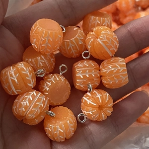 Close-up of orange pumpkin-shaped charms with white carved lines for DIY jewelry