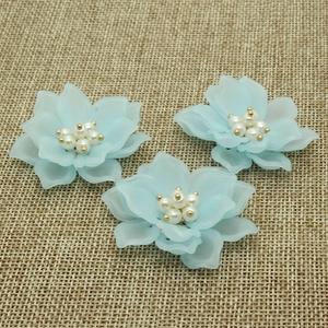 Tre toppe a forma di fiore di camelia in resina azzurra con perle su sfondo di lino rustico