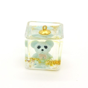 Detail of transparent resin cube pendant with blue bear and gold flakes inside