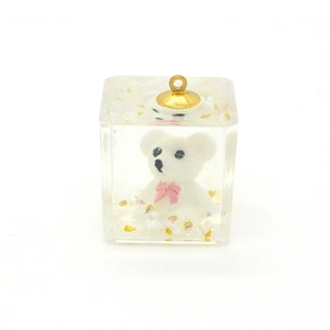 Detail of clear resin cube pendant with a white teddy bear and golden sequins inside