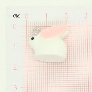 Close-up of small white rabbit pendant with pink ears on a centimeter measurement grid