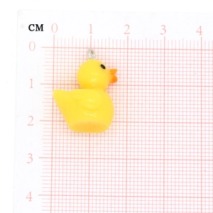 Close-up of a small yellow duck pendant showing size dimensions on a cm scale ruler
