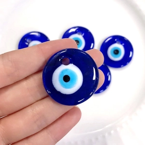 Handheld view of five blue glass Evil Eye charms with holes for DIY jewelry making
