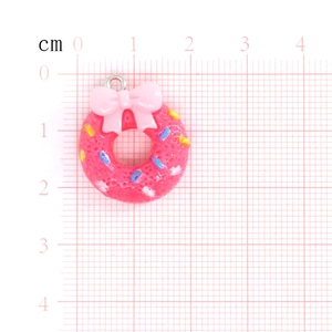 Pink resin donut pendant with bow and colorful sprinkles shown with size scale