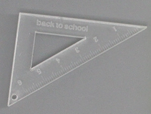 Close-up of a clear acrylic triangle ruler charm with 6cm scale and back to school text