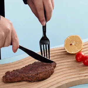 Black disposable plastic cutlery set cutting steak on wooden board with lemon details