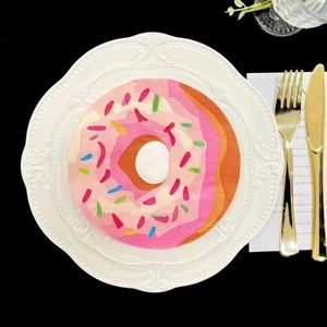 Pink donut shaped paper napkin with colorful sprinkles on a white ceramic plate
