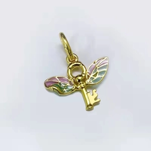 Détail d'un pendentif clé volante dorée avec des ailes en émail coloré et design gravé