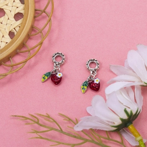 Silver strawberry charms with red enamel and white flower on pink textured background