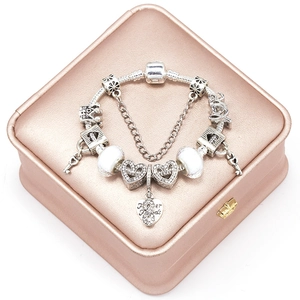 Silver charm bracelet with heart and crown pendants on a rose gold jewelry box