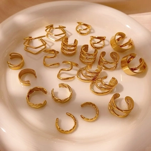 Set di ear cuff dorati geometrici con linee curve e texture ondulate su vassoio