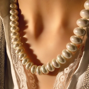 Gros plan d'un collier de perles élégant aux reflets irisés sur un costume vintage