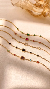 Detailed macro view of five thin gold link bracelets featuring colorful square gemstones