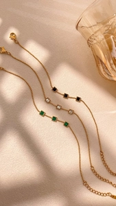Close-up of gold geometric chain bracelets with black, clear, and emerald green stones