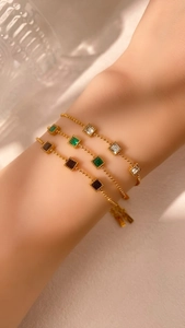 Detail of delicate gold bead bracelets with emerald, black, and clear square gemstones