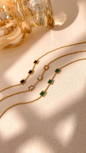 Detailed view of three gold bead bracelets with square black, white, and green gems