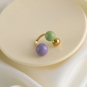 Dettaglio di un anello aperto con perle sferiche viola, verdi e dorate su un vassoio elegante