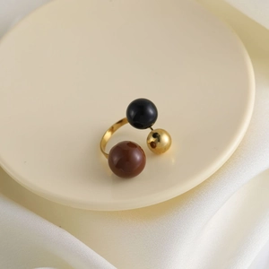 Dettaglio anello aperto dorato con tre perle lucide in nero, marrone e oro elegante