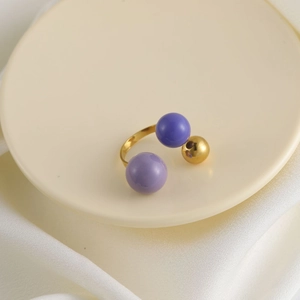 Dettaglio anello elegante placcato oro con perline viola su espositore crema