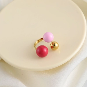 Dettaglio macro di un anello aperto con ciondoli a sfera rossi, rosa e dorati vivaci