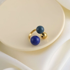 Dettaglio macro di un anello elegante con sfere blu e oro su un tessuto di raso