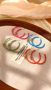 Detail of colorful C-shaped lacquer hoop earrings with square zircon on linen