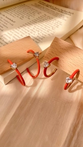 Detailed view of orange enamel C-shaped earrings with heart-shaped zircon on wood