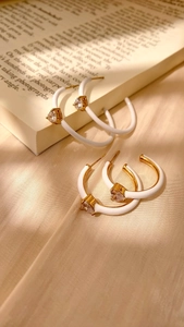 Detail of gold C-shaped enamel earrings with sparkling heart-shaped zircon stones