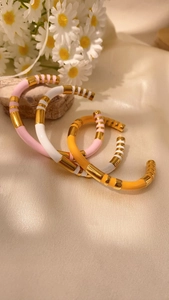 Dettaglio di tre bracciali smaltati stile bambù nei colori rosa bianco e giallo a forma C