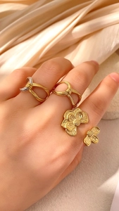 Nahaufnahme von großem unregelmäßigem Goldblumenring und gedrehten Bandringen an Fingern