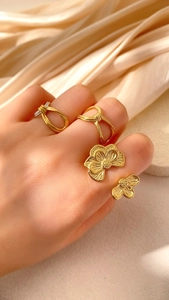 Nahaufnahme goldener Blumenring und geometrische Stapelringe auf Champagner-Satin