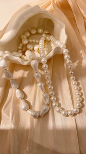 Primer plano detallado de collares de perlas redondas y barrocas en una bandeja de caracola