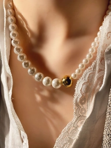 Detalle de collar de perlas elegante con una cuenta dorada pulida sobre encaje blanco