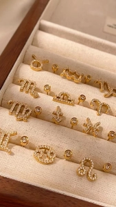 Gros plan de boucles d'oreilles zodiaque dorées serties de zircons en écrin de luxe