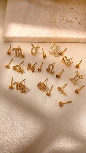 Détail de boucles d'oreilles zodiaque dorées avec pavé de zircons sur tissu en satin
