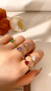 Dettaglio di cinque anelli con pietre preziose a cuore in vari colori e finitura oro