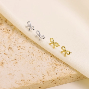 Elegant gold and silver bow stud earrings displayed on smooth fabric and stone surfaces
